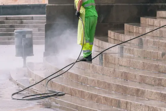 A worker pressure washing wide stone steps, mist rising off the treads