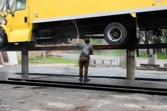 A worker washing down the side of a yellow box truck on a wash pad