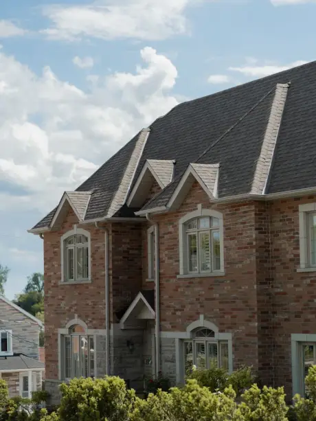 A brick home with a steep architectural shingle roof